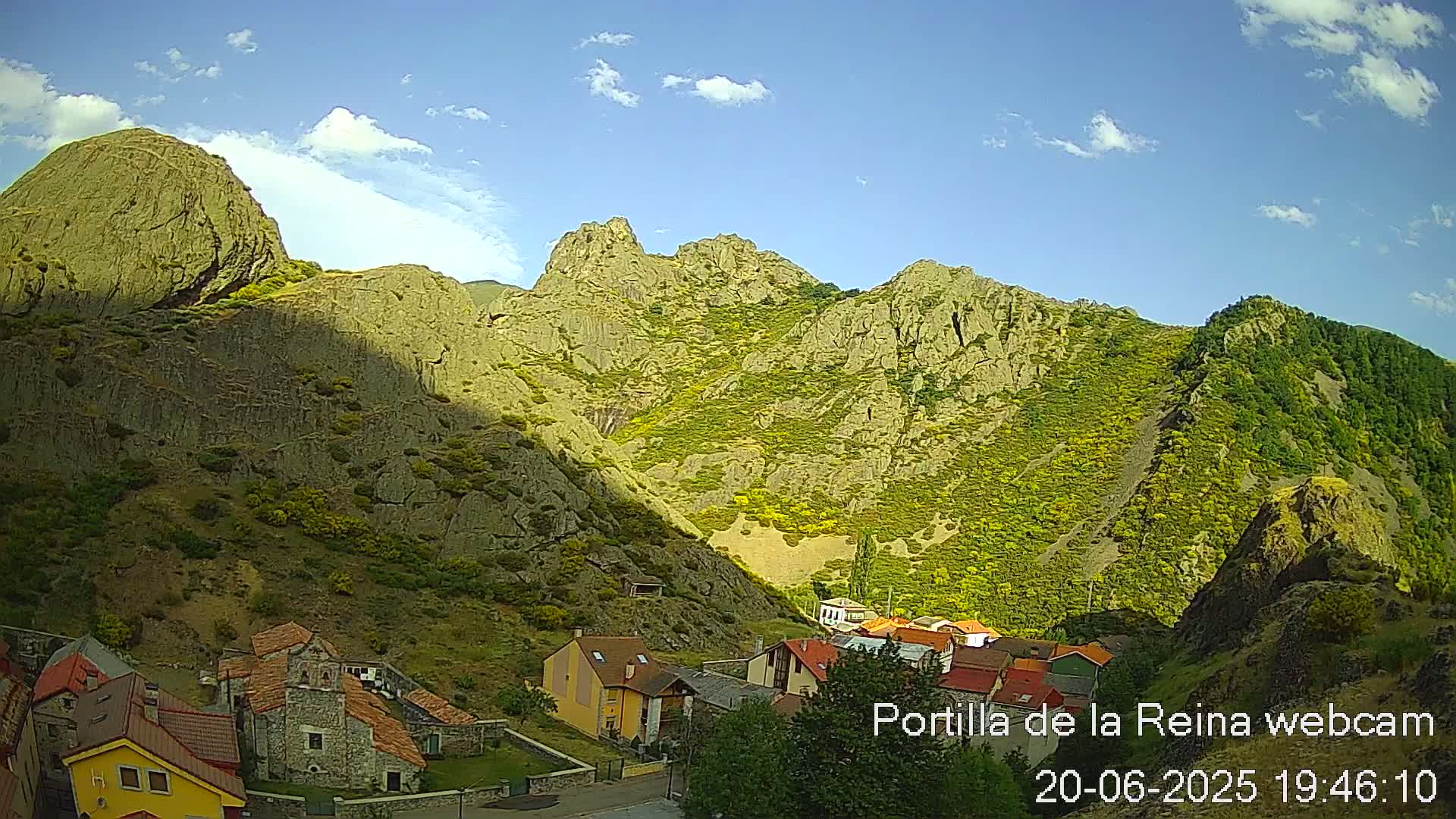 A small village nestled in a valley between steep, rocky mountains under a mostly sunny sky with a few clouds.