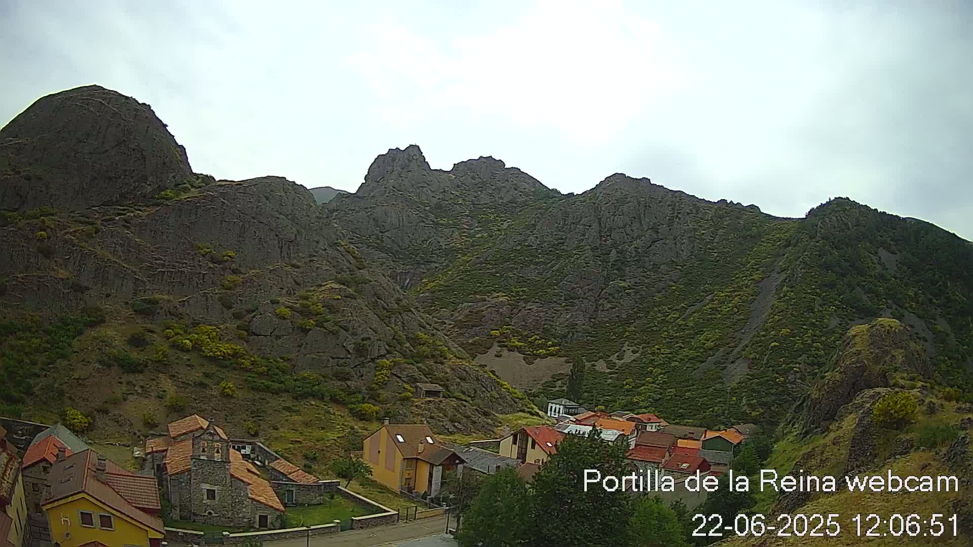 A small village nestled in a valley surrounded by large, rocky mountains under an overcast sky.