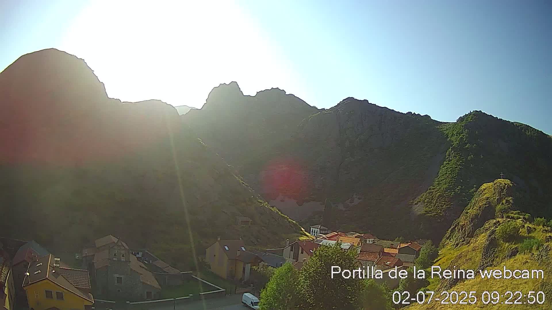 A small village nestled in a valley between sunlit, rocky mountains on a clear day.