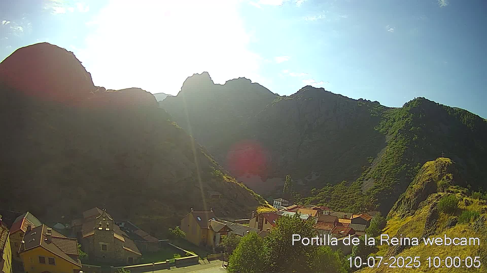 A sunny day reveals a small village nestled in a valley surrounded by steep, rocky mountains.
