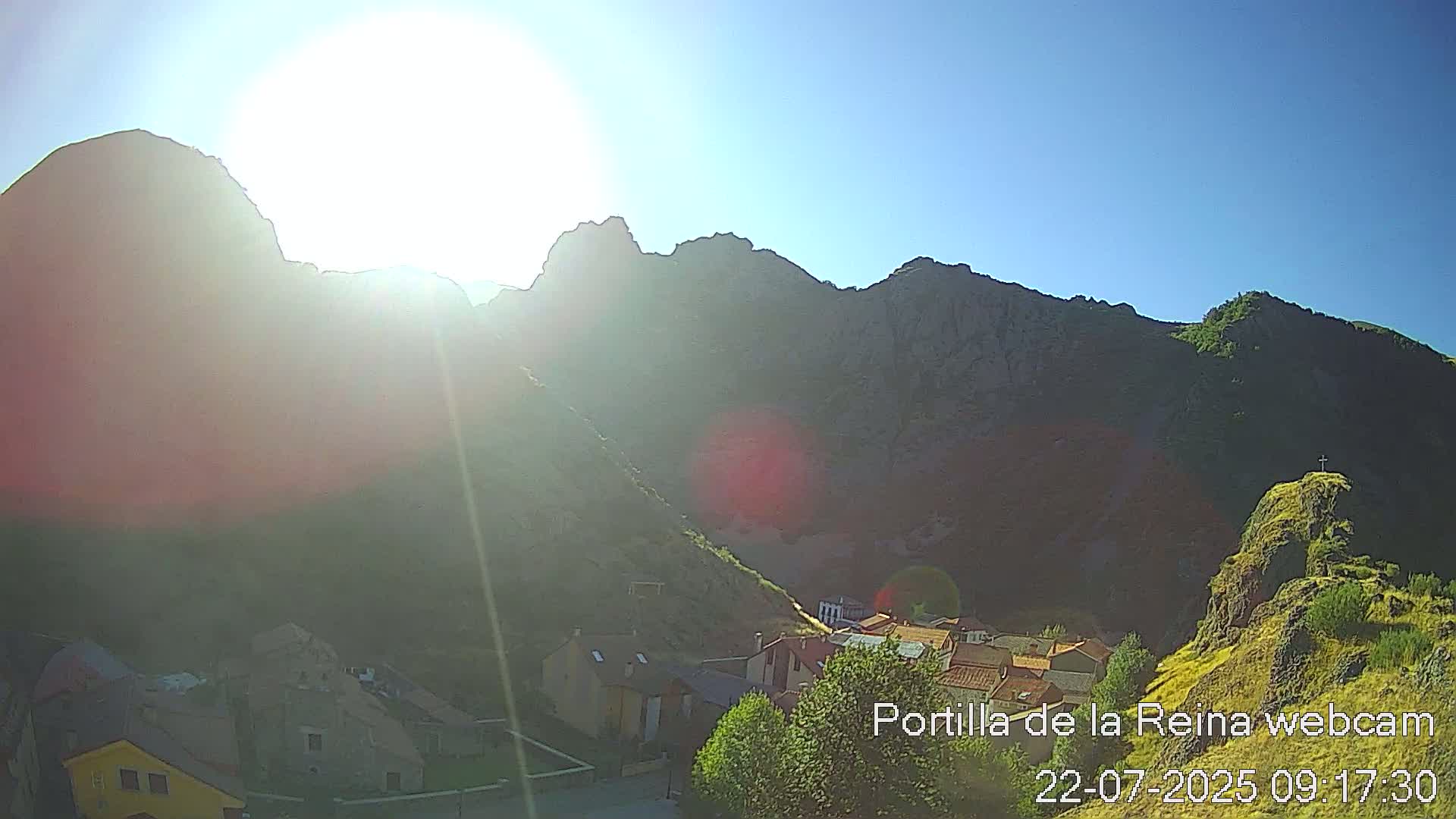 A small village nestled in a valley between sunlit, rocky mountains on a clear, sunny day.
