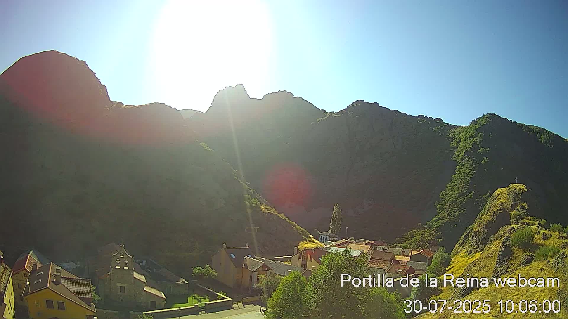 A sunny day reveals a small village nestled in a valley surrounded by large, rocky mountains.