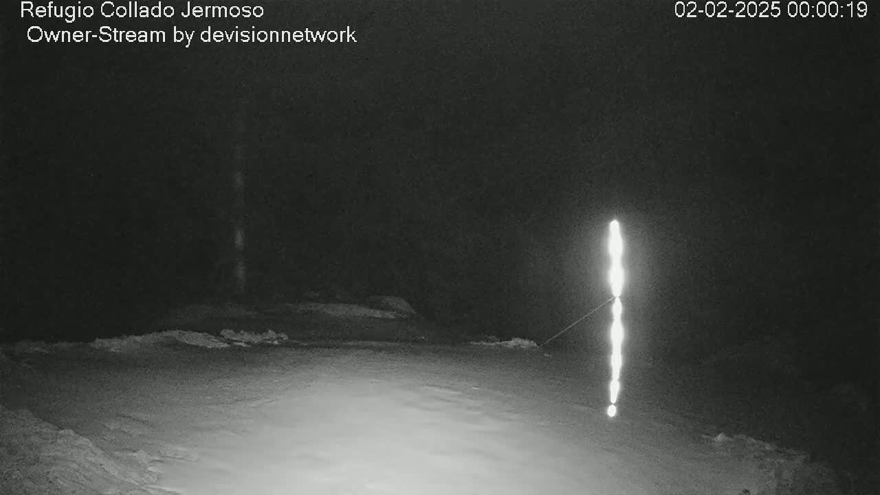 A nighttime, snowy scene shows a bright, vertical light source in the distance.