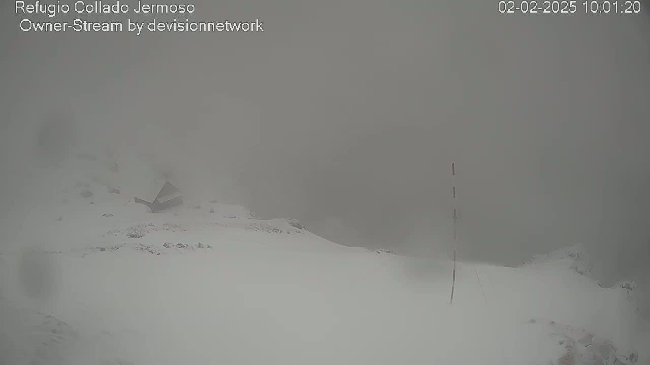 A snow-covered landscape is shrouded in thick fog, with a small structure partially visible in the mid-ground.