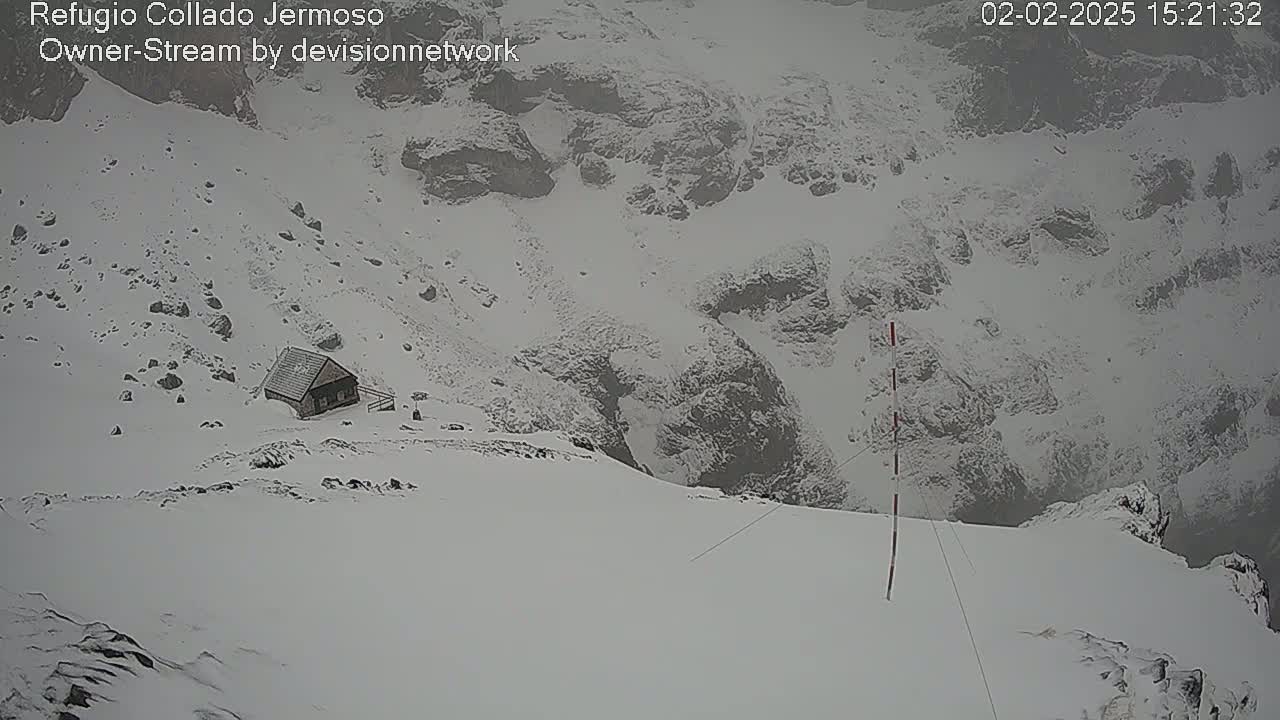 A small cabin sits on a snow-covered mountainside during a snowstorm.