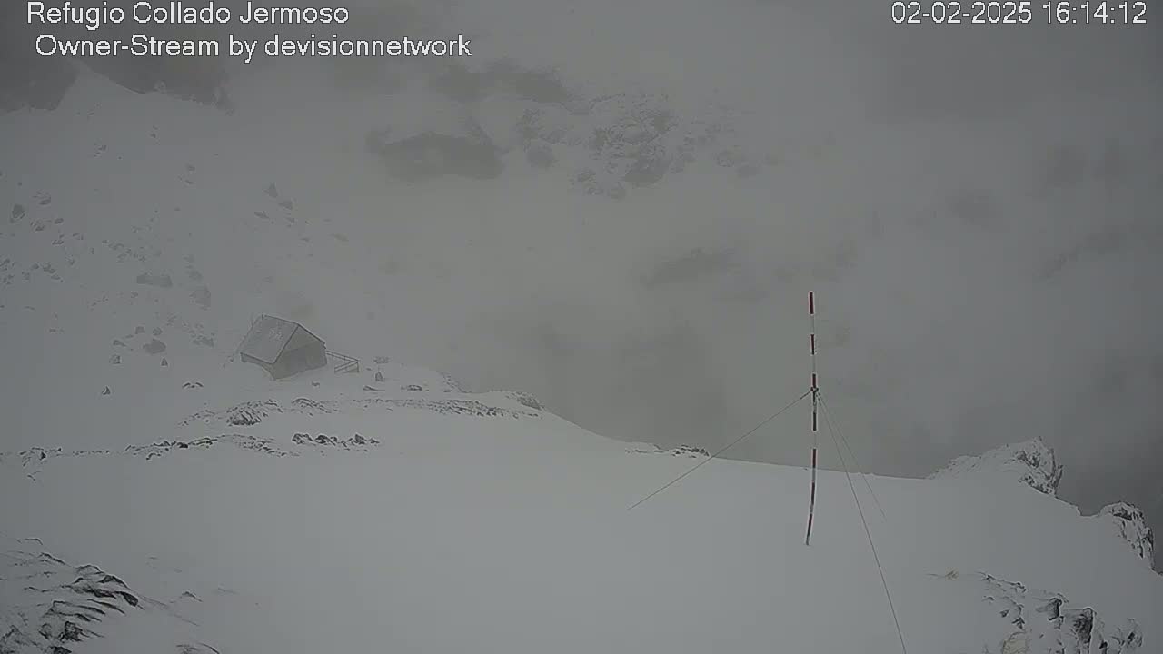 A small structure sits on a snow-covered mountaintop in foggy, snowy conditions.