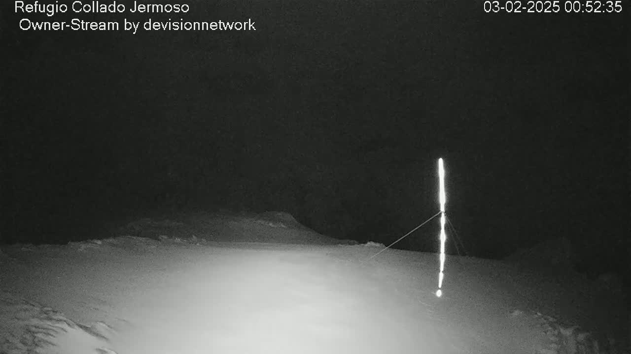 A snow-covered landscape is illuminated at night by a tall, thin light source.