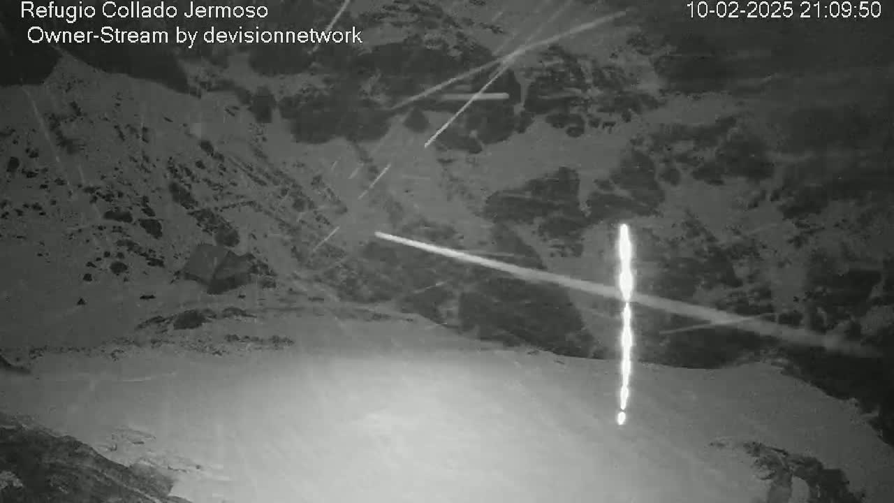 A nighttime, snowy mountain landscape is shown with several bright streaks across the sky, possibly meteors.