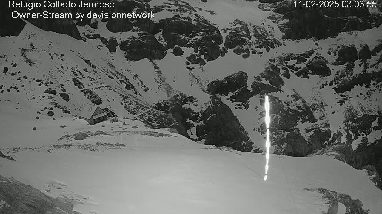 A small building sits on a snow-covered mountainside, with a bright vertical streak visible in the snow below.