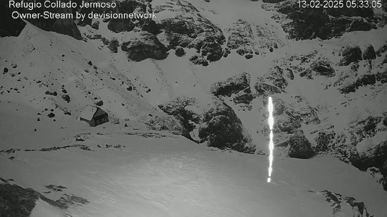 A small cabin sits nestled in a snow-covered mountainous region, with a bright vertical streak visible in the mid-ground.