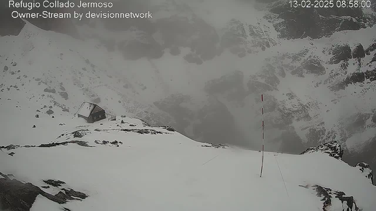 A small cabin sits on a snow-covered mountainside in foggy conditions.