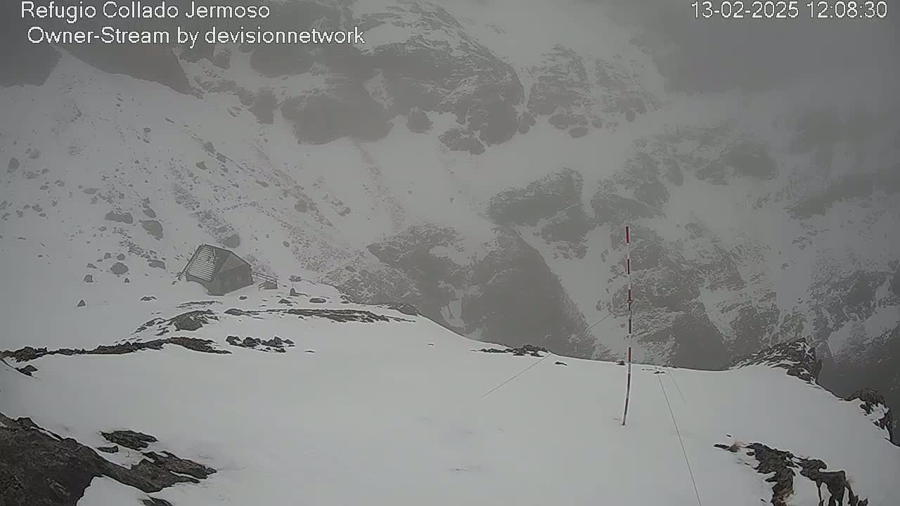 A snow-covered mountain landscape is visible in foggy conditions, with a small building nestled on the lower slope.