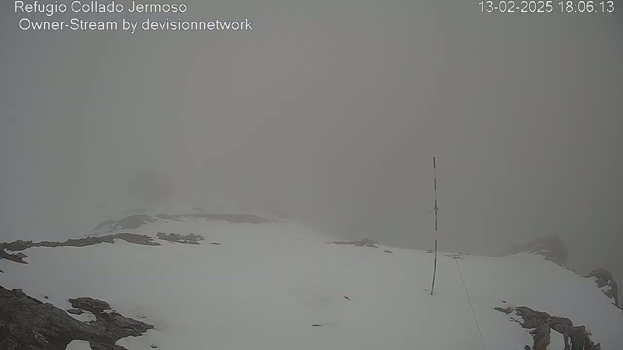 A snow-covered, rocky landscape is shrouded in thick fog.