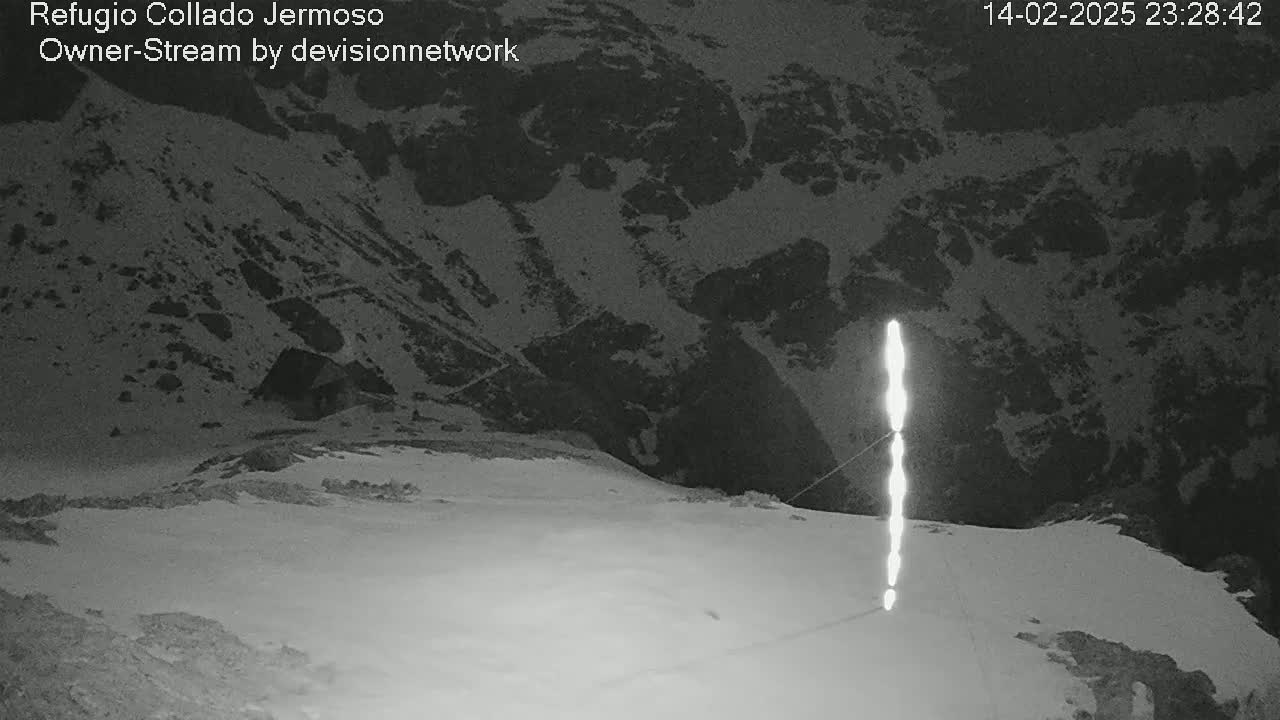 A nighttime, snowy mountain scene shows a bright vertical light source in the foreground with a dark, snow-covered mountain in the background.