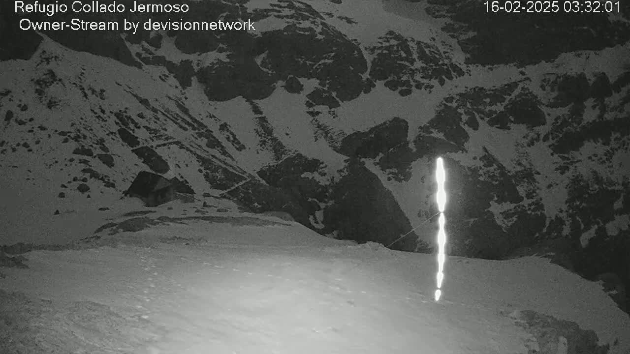 A nighttime, snowy mountain landscape is shown with a bright vertical light source in the middle ground.