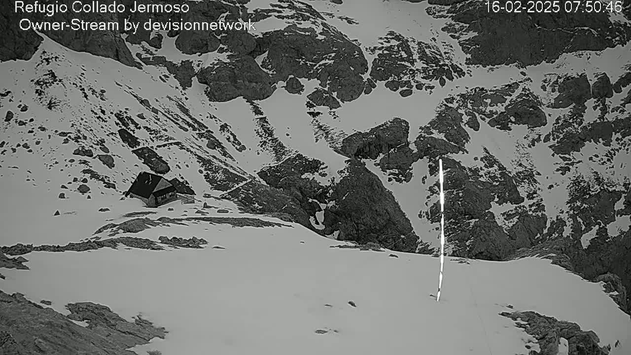 A small building sits nestled in a snow-covered mountainous region, with a bright vertical line visible in the snow.
