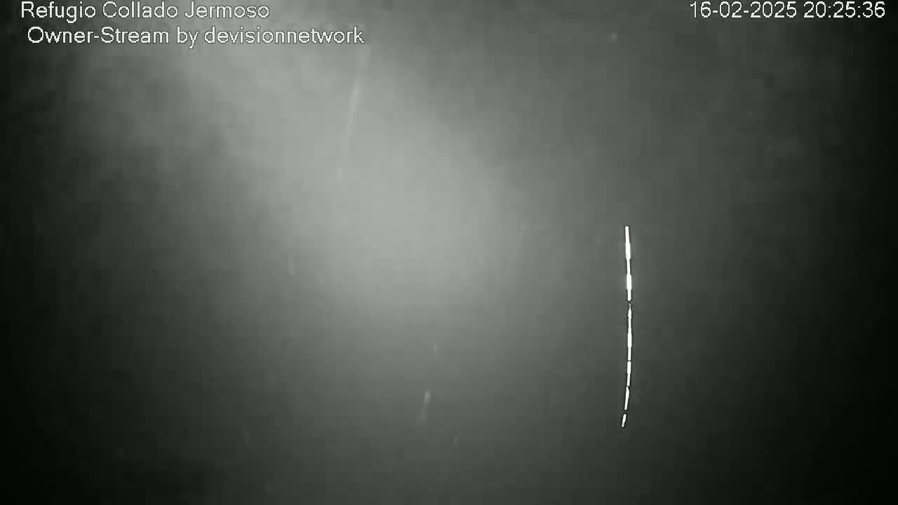 A grainy, dark gray image shows a thin, vertical line of bright light against a hazy, possibly snowy night sky.