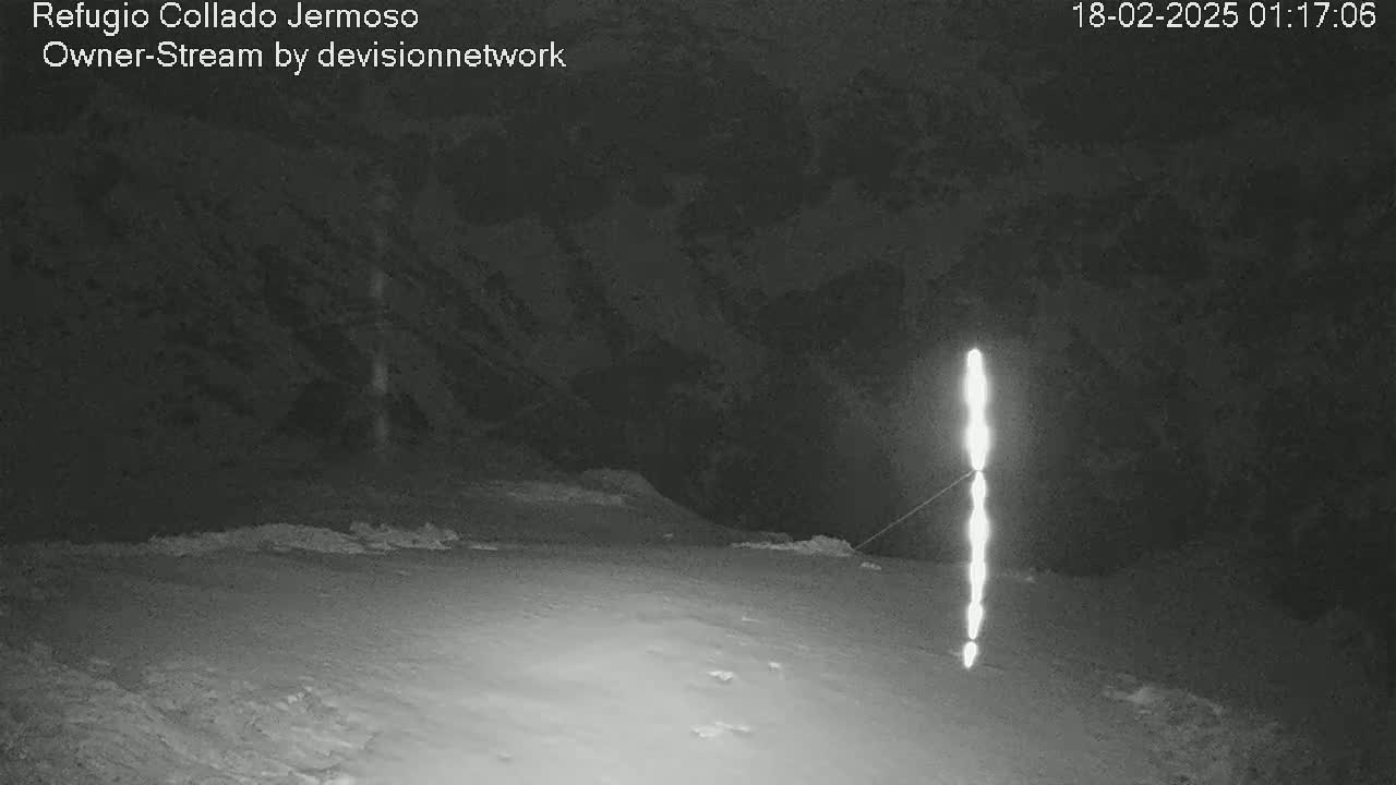 A nighttime, snow-covered landscape is illuminated by a vertical line of bright lights extending from the ground to a dark hillside.