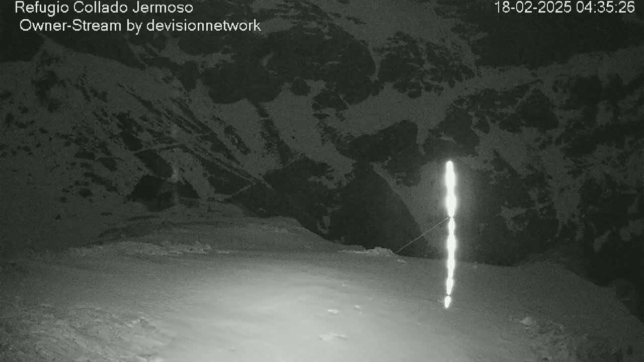 A nighttime, snow-covered landscape is shown with a bright vertical line in the foreground and a mountainous background.
