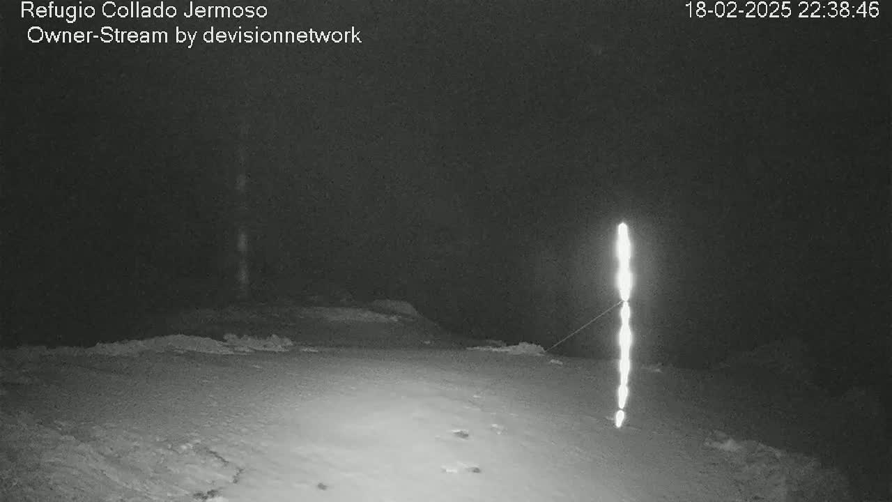 A nighttime, snowy scene shows a tall, bright light source in the middle ground.