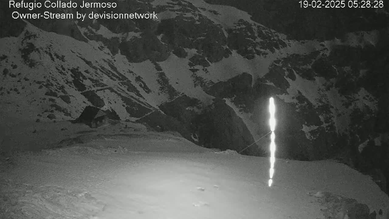 A nighttime, snow-covered mountain landscape is illuminated by a bright vertical light source.