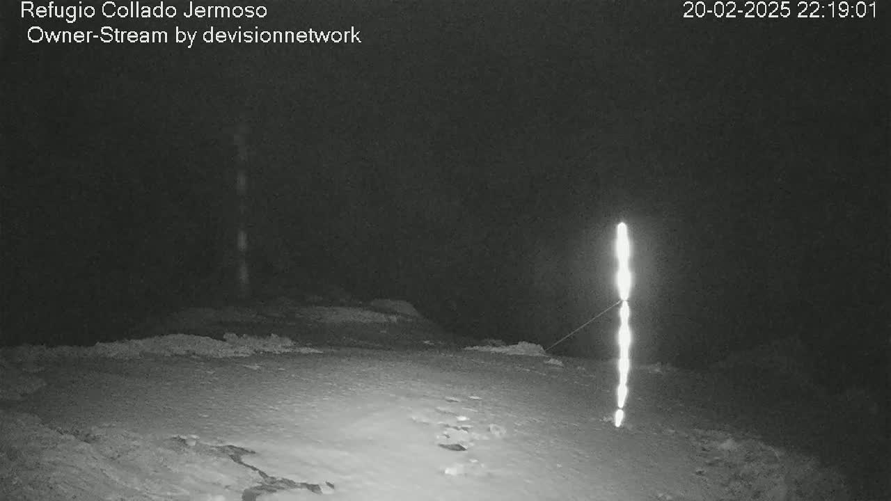 A nighttime, snowy scene shows a tall, thin, brightly lit object standing in the middle of a snow-covered ground.