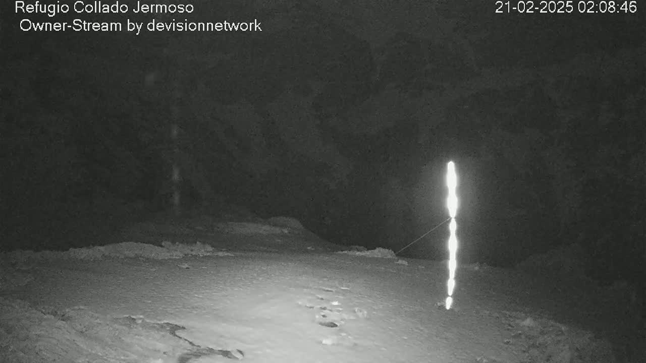 A nighttime, snow-covered landscape features a tall, slender, bright light source in the distance.