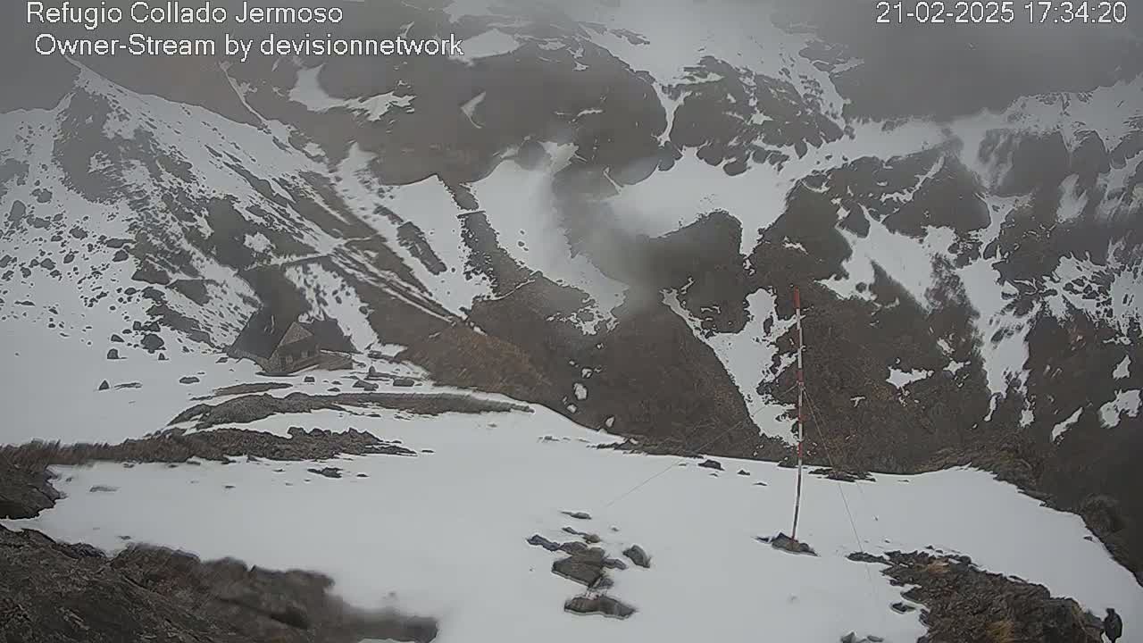 A snowy, foggy mountain landscape is seen from a high vantage point, with a small structure visible in the distance.