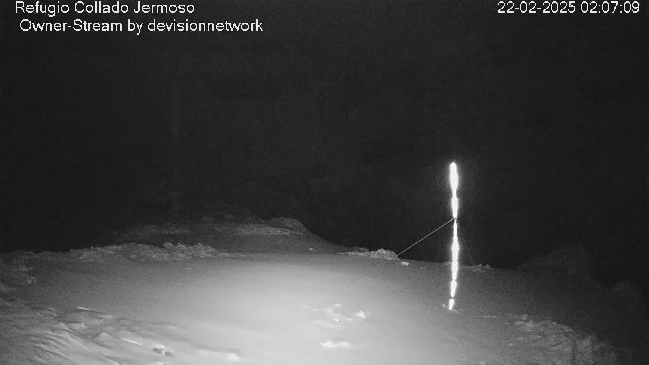 A snow-covered landscape at night is illuminated by a vertical light source attached to a thin wire.