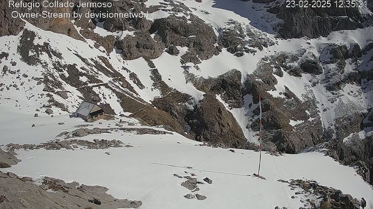 A small building sits on a snow-covered mountainside under sunny conditions.