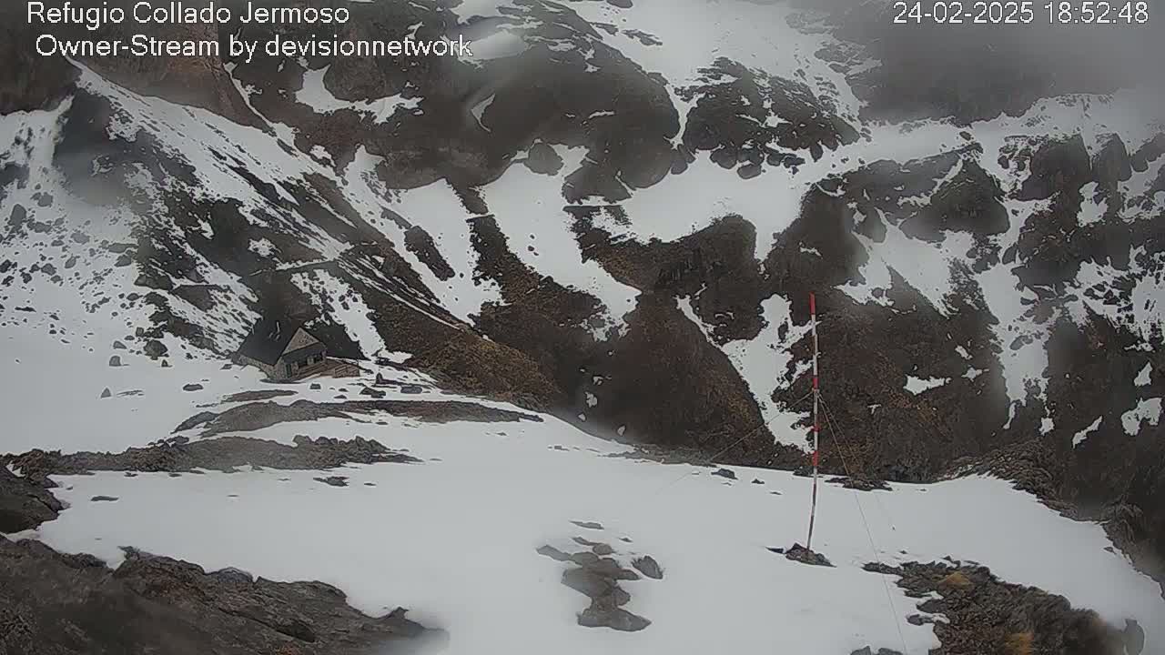 A snow-covered mountainside with a small building visible in the distance, under hazy or foggy conditions.