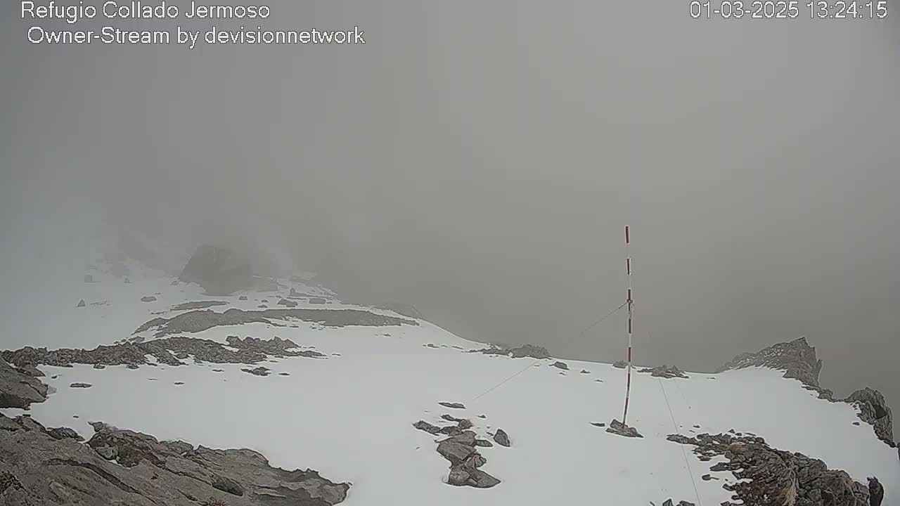 A snow-covered rocky mountain peak is shrouded in thick fog.