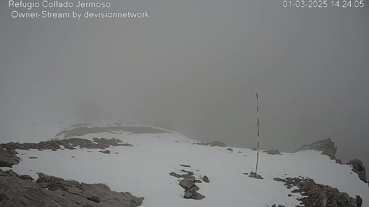 A snowy, rocky mountaintop is shrouded in thick fog.