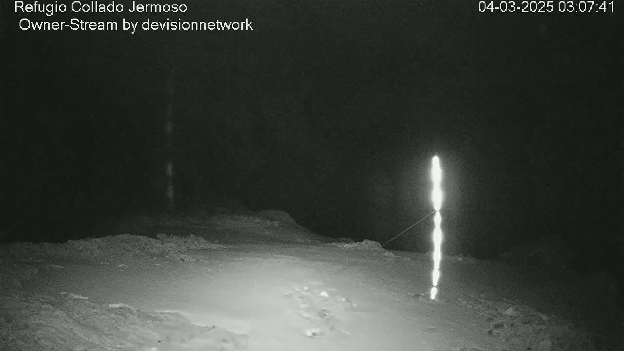 A snow-covered landscape is illuminated at night by a tall, vertical light source.