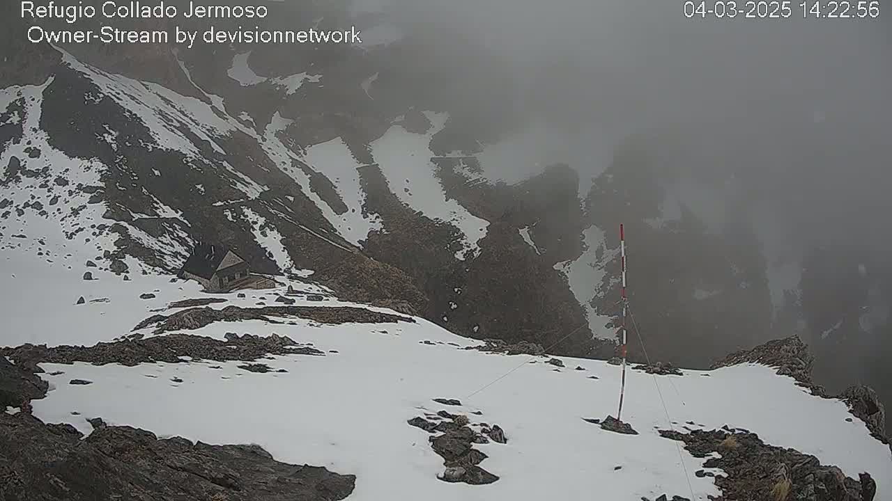 A snow-covered mountain peak with a small building visible in the distance, shrouded in fog.