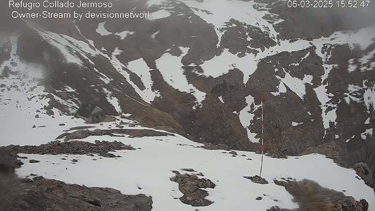A snowy, mountainous landscape is shown under overcast skies, with a small structure visible in the distance.