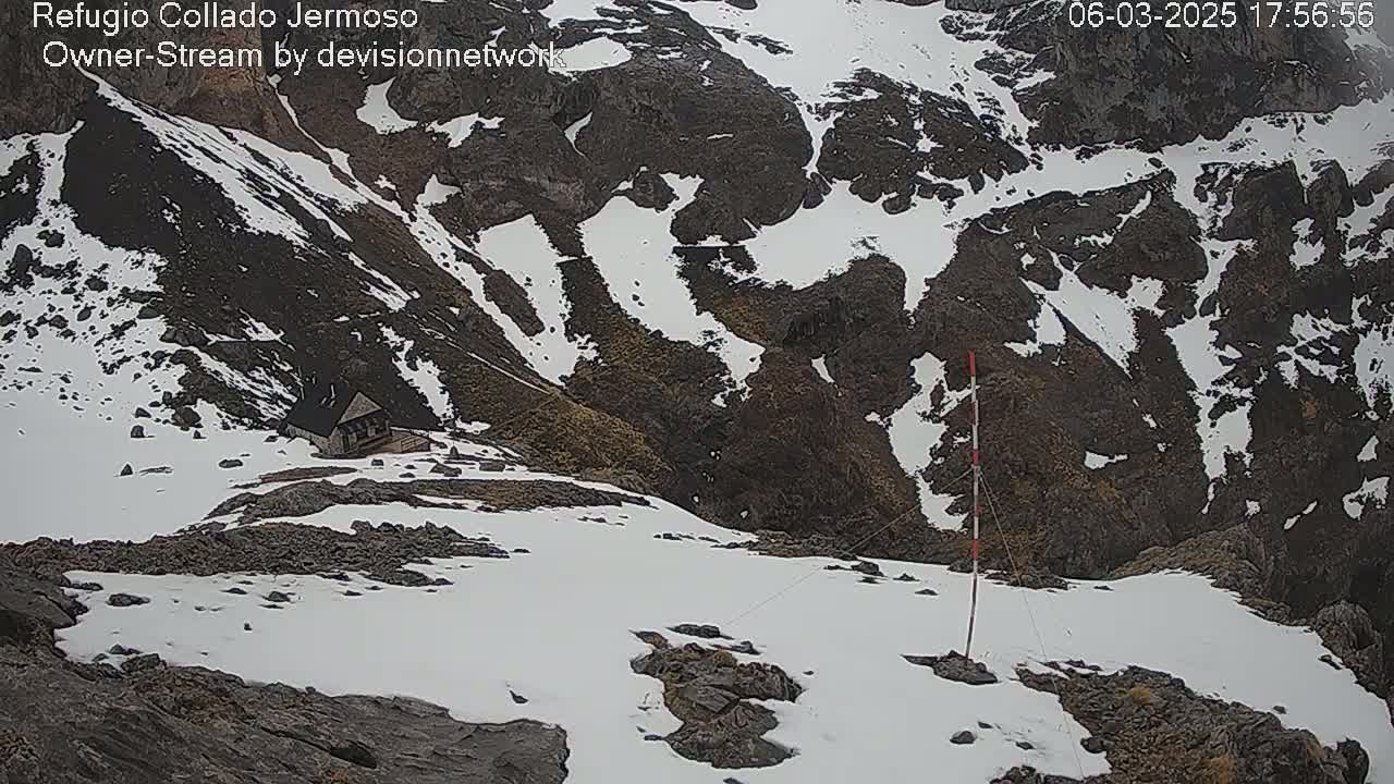 A small cabin sits nestled in a rocky, snow-dusted mountainside.