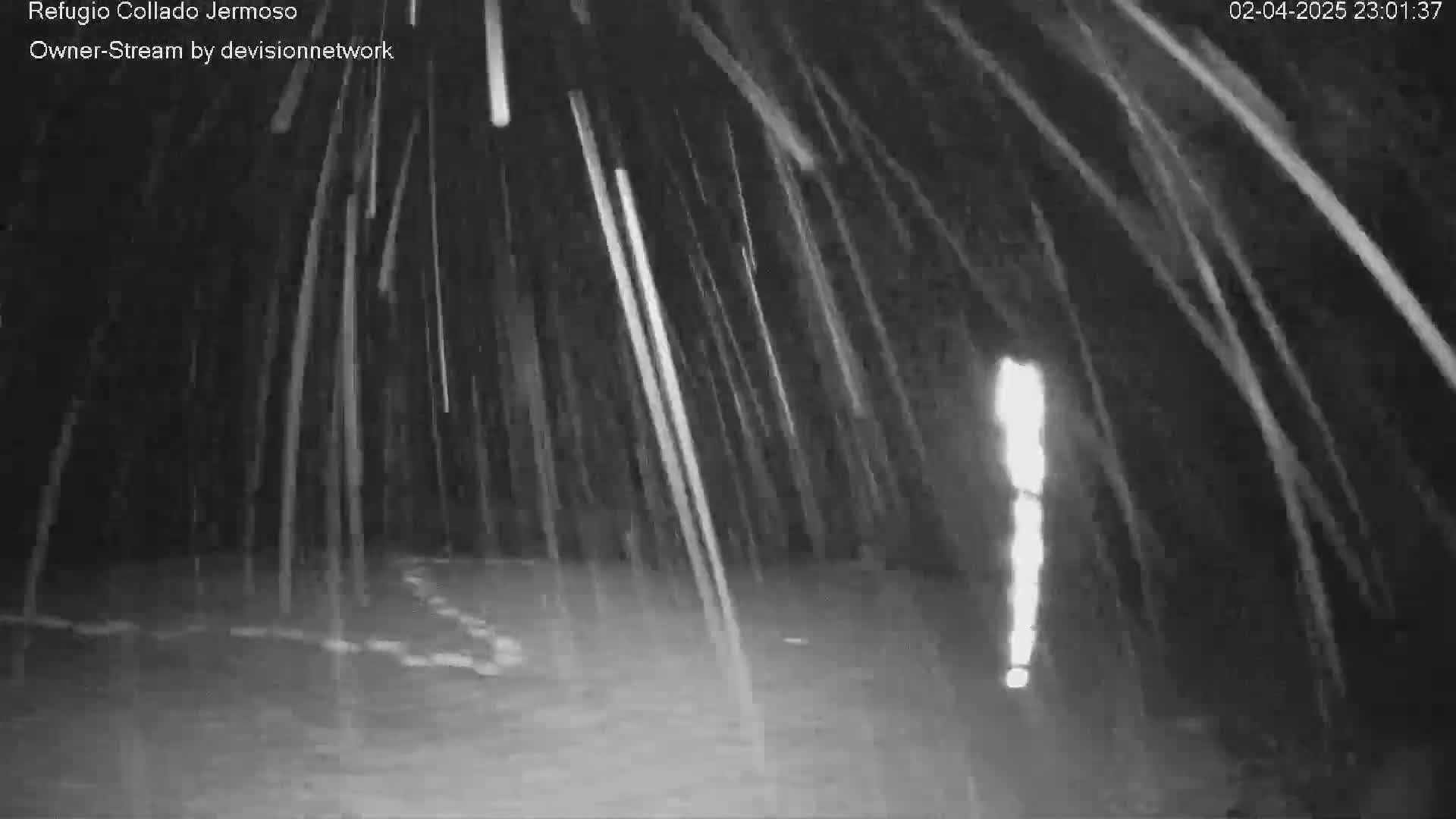 A nighttime, black and white image shows heavy rain falling over a dark, possibly flooded area.