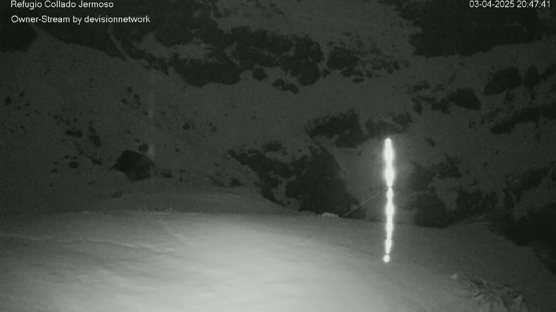 A nighttime, snow-covered landscape is illuminated by a vertical line of bright light.