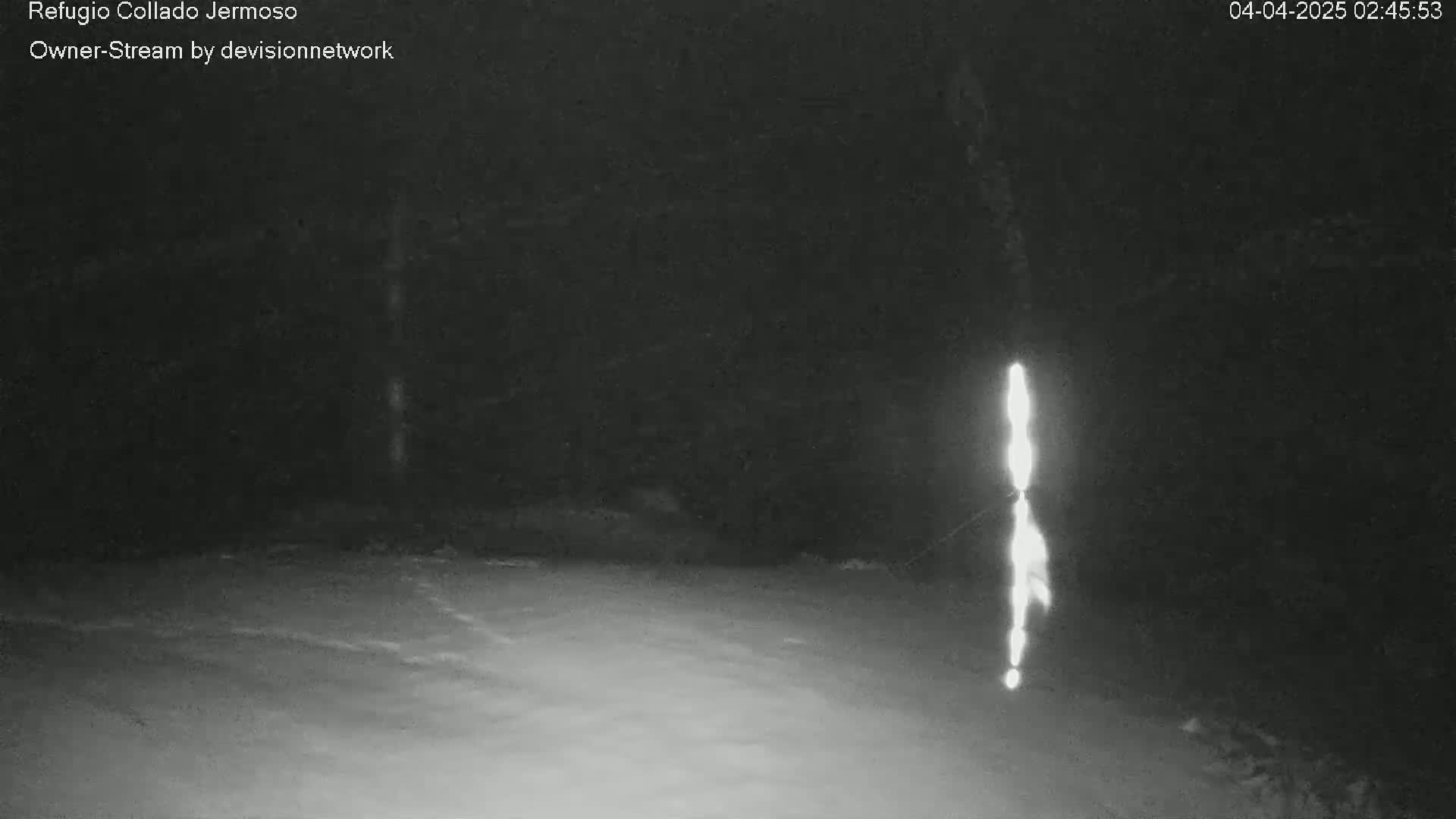 A bright vertical light source is visible in the center of a dark, snowy nighttime scene.