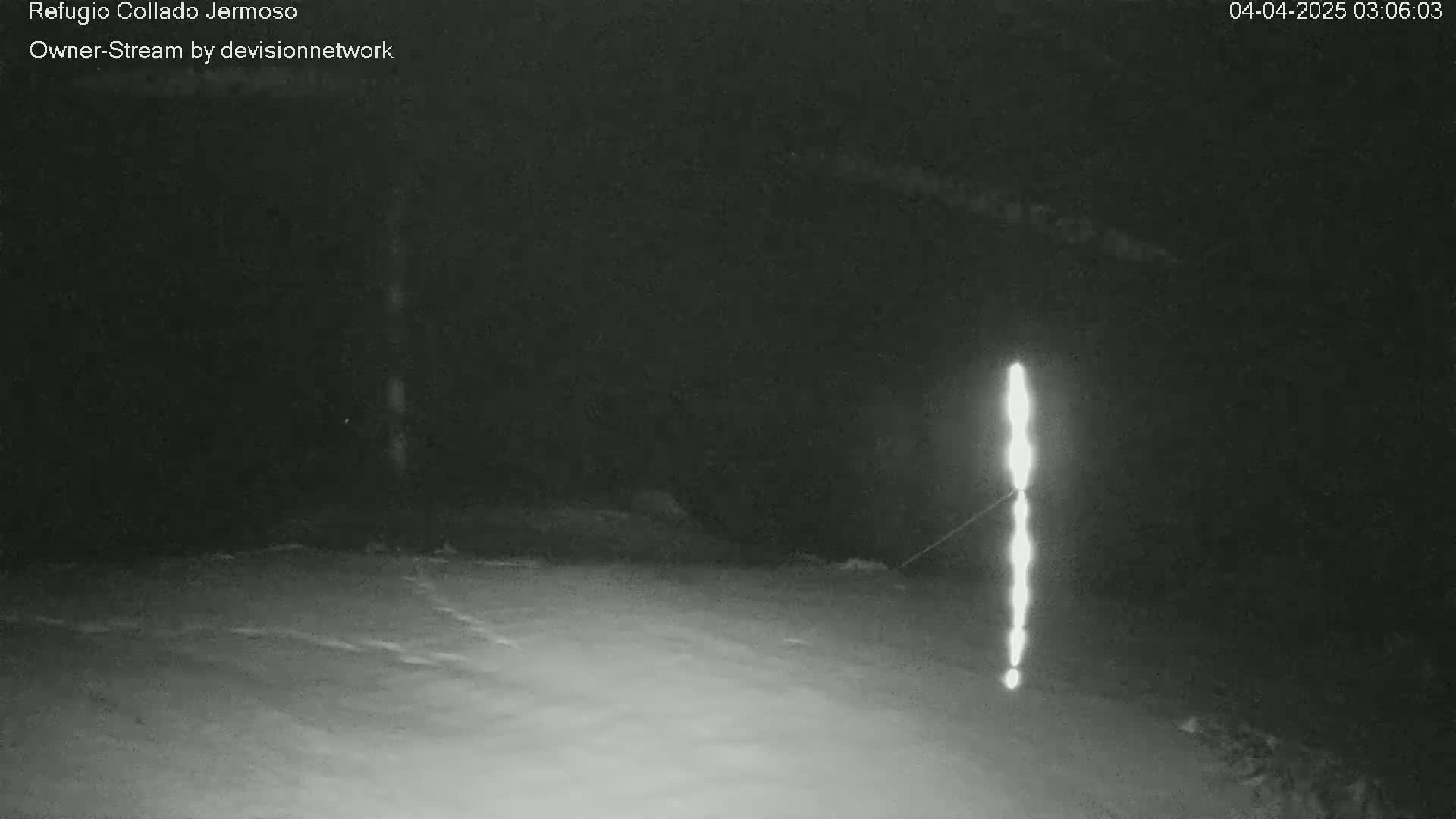 A bright vertical light source is visible in the distance against a dark, snowy nighttime landscape.