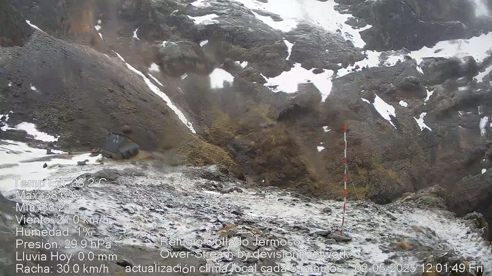 A rocky, snow-dusted mountain landscape with a vehicle visible near the bottom, under slightly overcast skies.