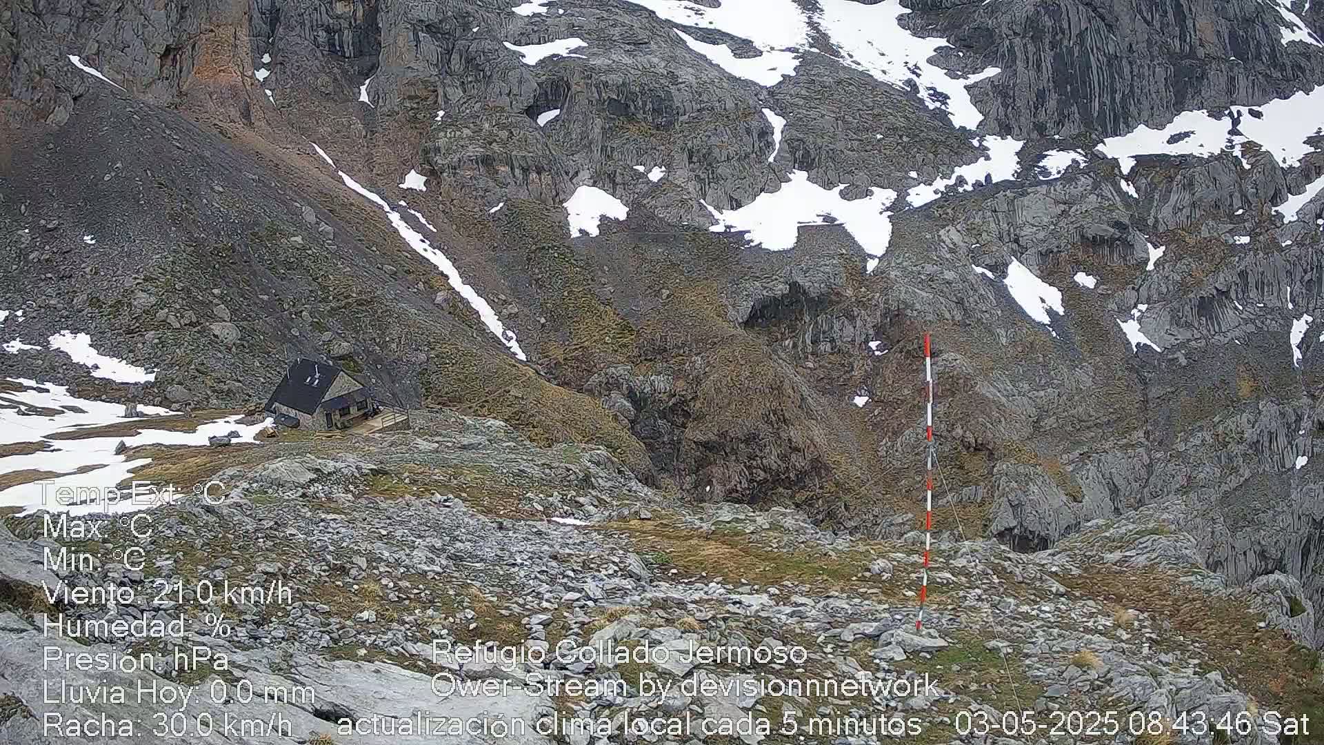 A small cabin sits on a rocky, snow-dusted mountainside.