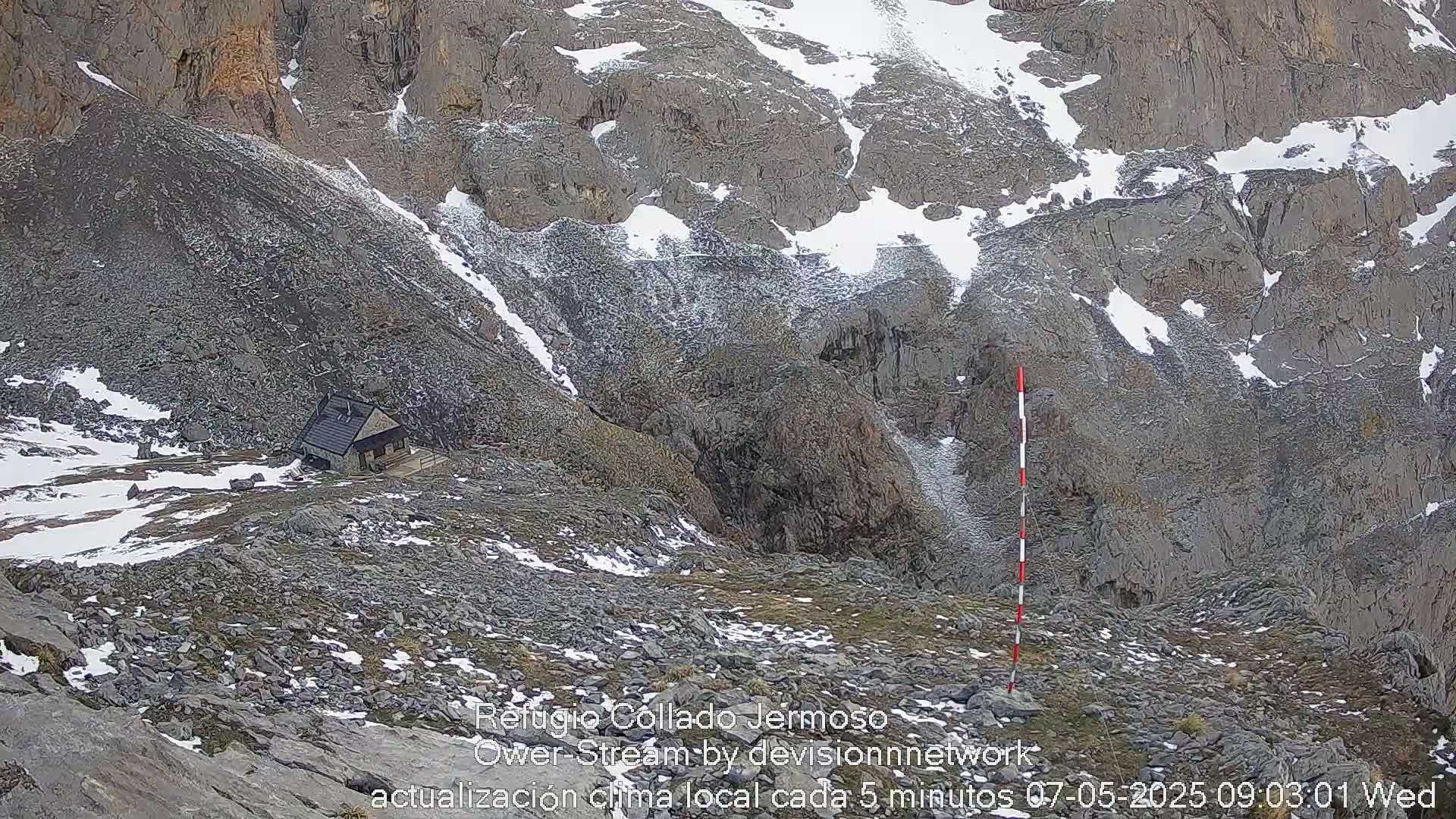 A small building sits on a rocky, snow-dusted mountainside.