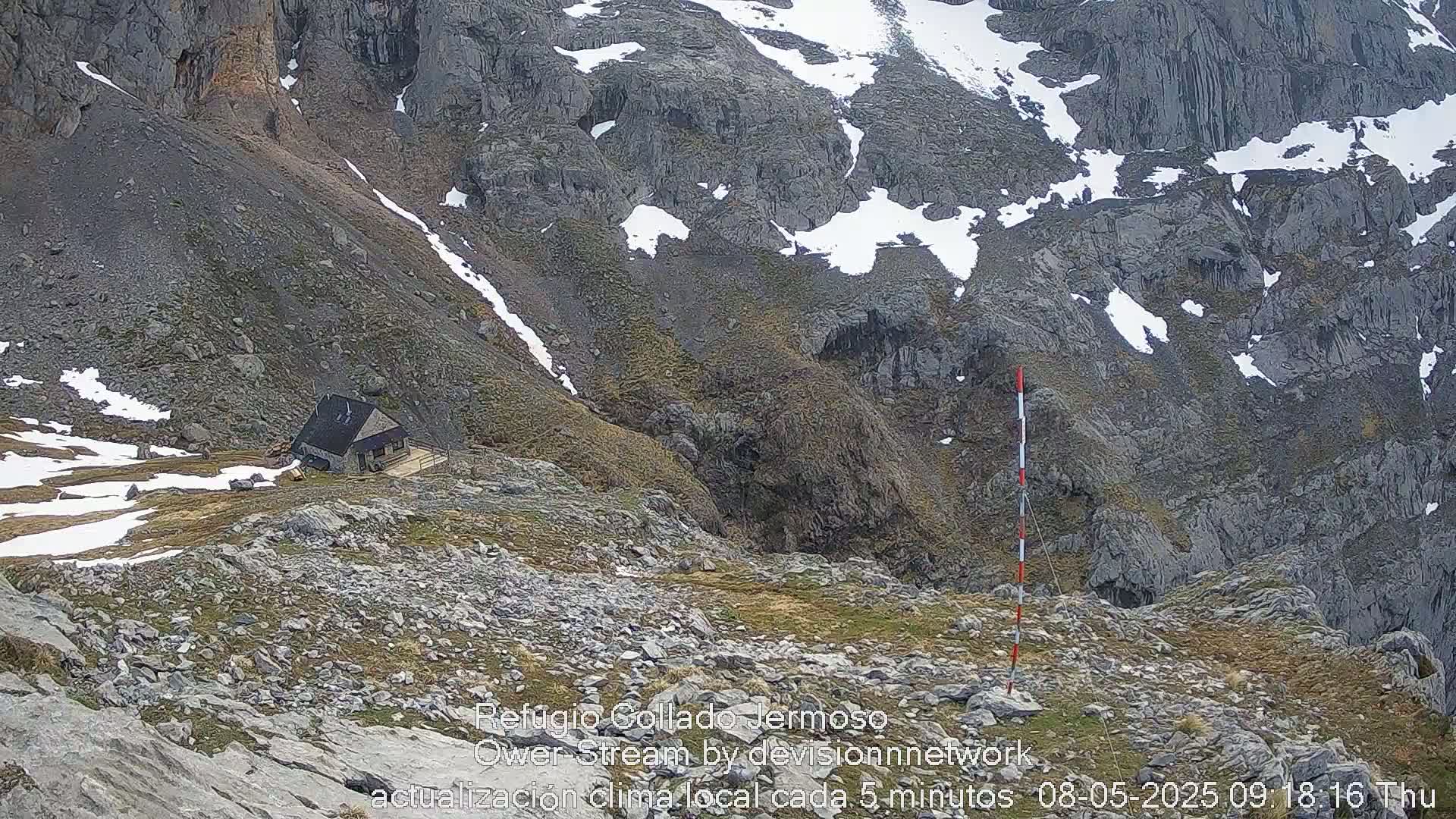 A small cabin sits on a rocky, snow-dusted mountainside.