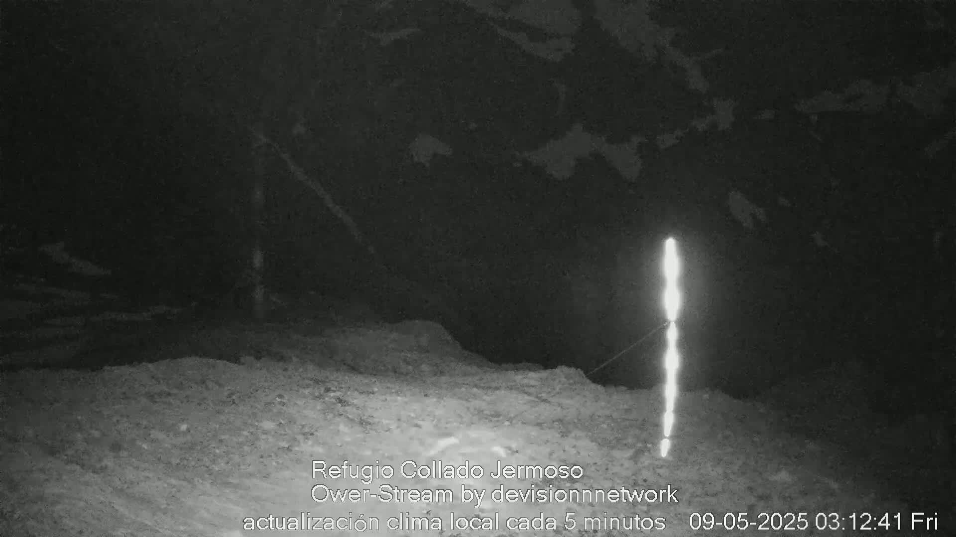 A nighttime, low-light image shows a rocky, uneven ground with a bright vertical light source in the right side of the frame.