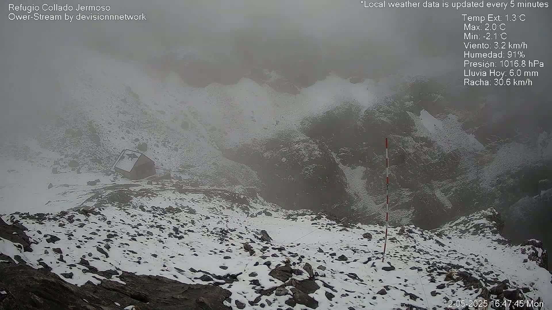 A snow-covered rocky mountain landscape is partially obscured by fog, with a small building visible in the mid-ground.