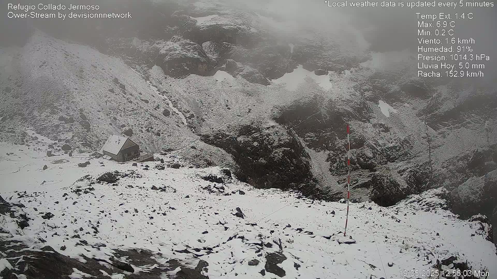 A snow-covered mountainous landscape features a small cabin, with foggy conditions.