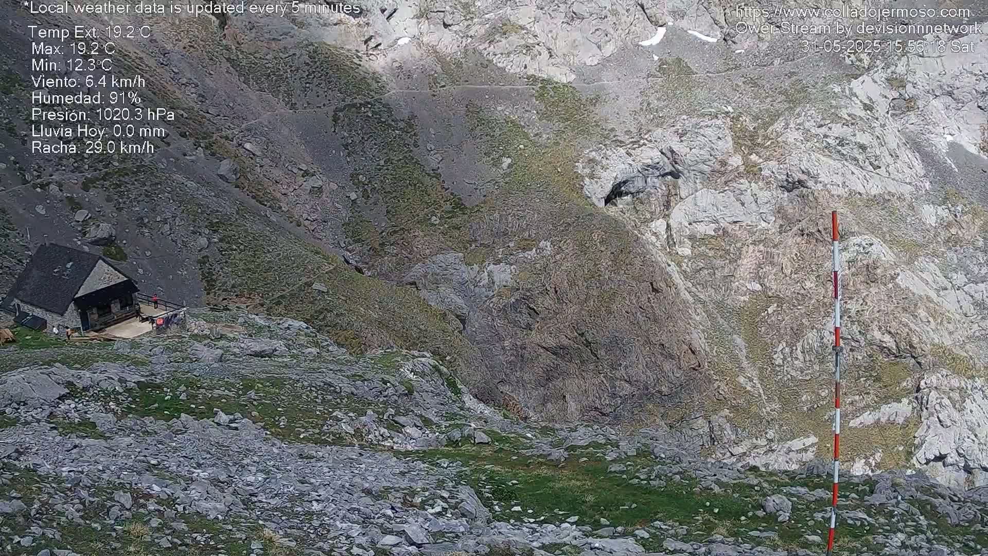 A stone hut sits on a rocky, grassy mountainside under a clear sky.
