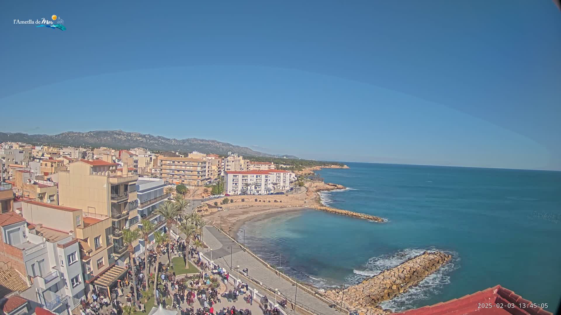 A coastal town with a sandy beach and calm, clear blue water under a sunny sky.